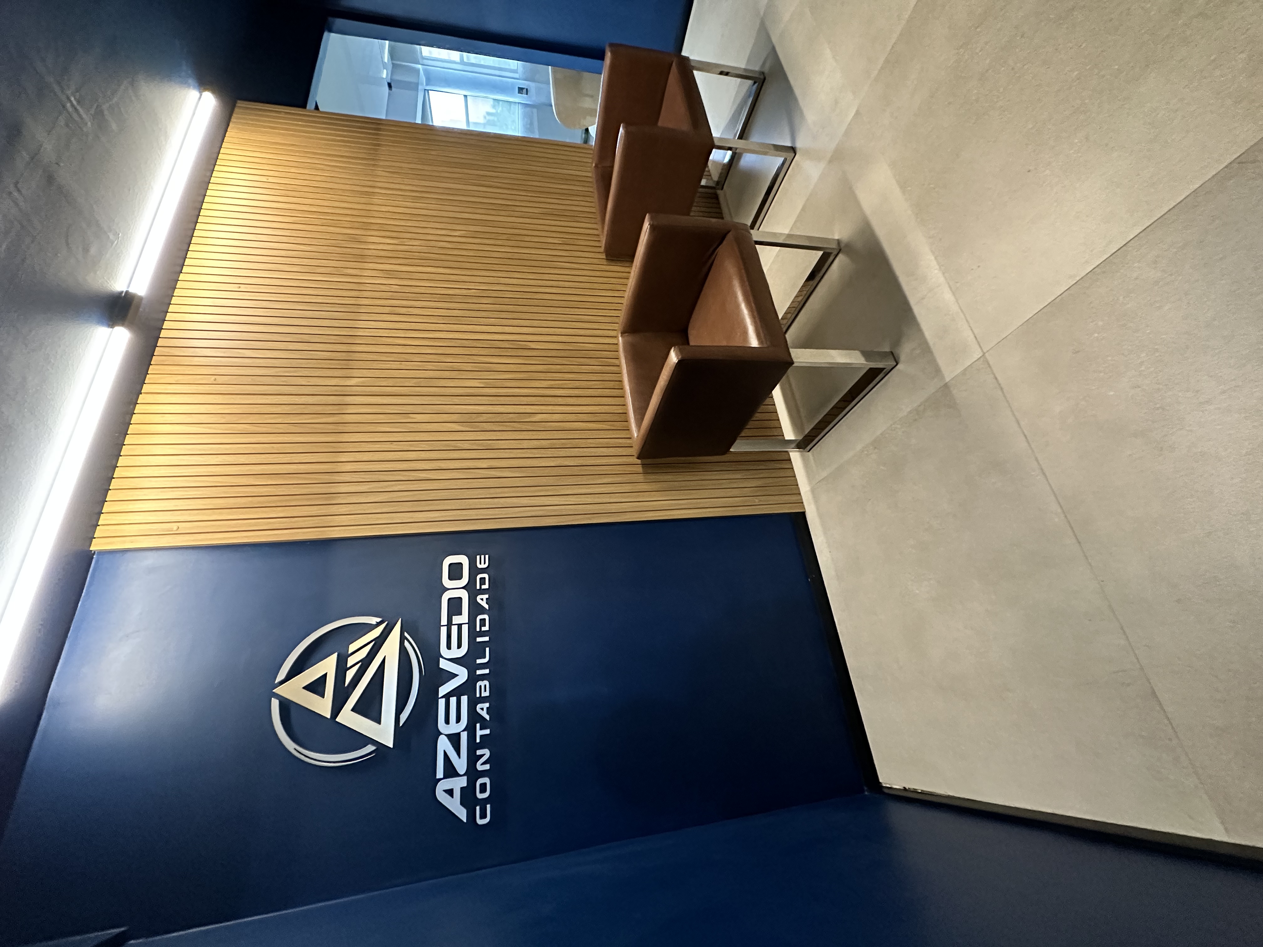 Recepção Azevedo Contabilidade - Logo na parede azul marinho com poltronas de couro